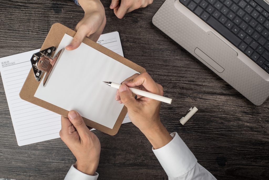 Close-up top view of two people reviewing a construction contract checklist on a clipboard.